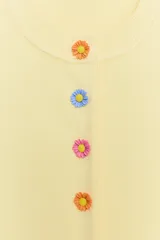 Chaqueta de punto color amarillo claro, con cuello redondo y manga corta. Presenta cierre frontal con botones de presión con diseño de flores de colores.