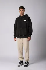 Buzo canguro oversize de algodón frisa premium con efecto lavado en color negro. Presenta capucha, bolsillo frontal tipo canguro y estampa blanca en el pecho.