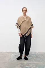 Poncho artesanal de lana en color beige, con diseño de textura rústica y terminaciones con flecos. Presenta una franja decorativa con patrón geométrico en tonos negros y blancos en el borde inferior.