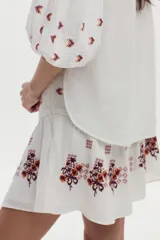 Falda corta blanca de gasa de algodón, con diseño evasé y detalles bordados florales en tonos marrón y naranja.
