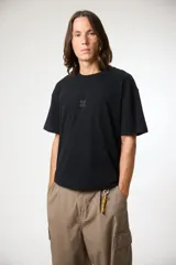 Remera de manga corta color negro, con corte holgado y diseño minimalista que presenta un pequeño logo bordado en forma de cruz en el centro del pecho.
