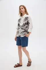 Camisa de viscosa de corte holgado, color blanco con estampado negro de paisaje con palmeras, cuello camisero y cierre frontal con botones.