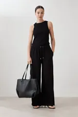 Pantalón de corte amplio y tiro medio, confeccionado en tejido suave de color negro. Presenta una cintura elástica con cordón ajustable y bolsillos laterales amplios.