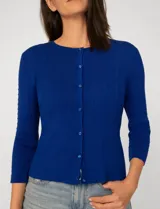 Cardigan blanco de tejido liviano con trama en relieve, cuello a la base y cierre frontal con botones a tono. Presenta mangas tres cuartos.