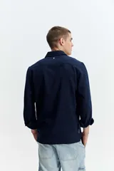 Camisa rústica de manga larga color gris oscuro, con cuello clásico, cierre frontal con botones y un bolsillo aplicado en el pecho.