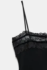 Top de tirantes finos confeccionado en tejido semitransparente, con escote recto decorado con encaje a tono, bordados florales y detalles de terciopelo con lazos. Presenta un diseño con abertura frontal y bajo con encaje.