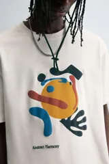 Camiseta de manga corta y cuello redondo, color blanco hueso, con un estampado abstracto multicolor en el pecho que incluye texto en la parte inferior.