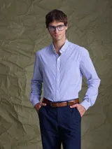 Camisa de manga larga con cuello abotonado y estampado de rayas verticales finas en tonos azul y blanco. Presenta un bolsillo frontal en el pecho y cierre de botones.