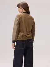 Chaqueta estilo bomber con diseño híbrido, combinando mangas y frente en tejido de lana con patrón de espiga en tonos tierra, y espalda en tejido liso de poliéster color marrón. Presenta puños y ruedo elásticos en color negro, brindando una estructura definida y un estilo contemporáneo.