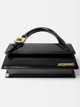 Bolso estructurado de cuero liso color negro, con asa superior reforzada, detalle de hebilla metálica dorada y logo de la marca en letras doradas en la parte frontal.