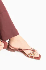Sandalia de cuero color caramelo, con tiras finas y detalle frontal trenzado en tonos marrón, celeste y naranja. Cuenta con pulsera ajustable con hebilla metálica y taco bajo geométrico.