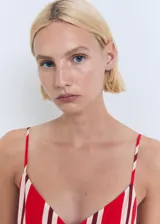 Mono largo de diseño recto con estampado de rayas verticales en rojo y blanco. Presenta cuello de pico, tirantes finos y aberturas laterales tipo cut-out en la cintura. Incluye cierre de cremallera en la parte posterior y forro interior.