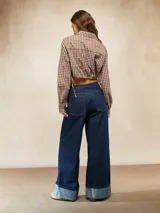 Camisa de manga larga, cuello camisero y botones frontales, con estampado a cuadros marrones y blancos. El ruedo inferior es ajustable con cordones laterales, creando un efecto *cropped* y fruncido.