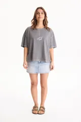Remera de algodón gris con efecto lavado, corte semi boxy, mangas cortas y costuras en contraste. Presenta un pequeño bordado frontal con líneas curvas y la palabra "Ciao".