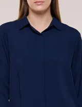 Camisa blanca de corte clásico y caída fluida, con cuello camisero tradicional, abotonadura frontal oculta y mangas largas con puños anchos.