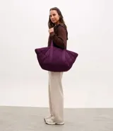 Cartera tipo shopper de gran tamaño con diseño acolchado puffer, confeccionada en poliéster. Presenta asas anchas de cinta de gorgorán para llevar al hombro y una estructura amplia en forma de trapecio invertido.