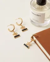 Aros tipo argolla de acero dorado con dije colgante en forma de estrella calada y barrita horizontal con detalle en esmalte negro.