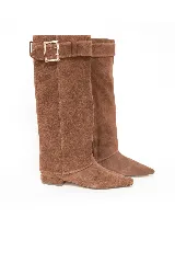 Bota de caña alta de gamuza color marrón, con punta fina, taco bajo y detalle de tira con hebilla metálica en la parte superior.