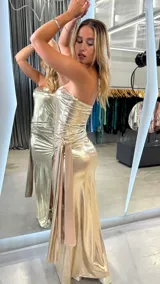 Vestido largo dorado metalizado, strapless, con drapeado lateral y abertura en la pierna. Incluye lazo lateral.