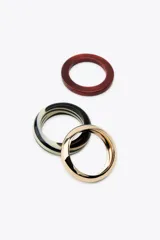 Pack de tres pulseras rígidas para mujer, una dorada metálica en relieve y dos de resina en color borgoña y negro con rayas blancas.