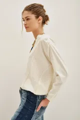 Remera de algodón color crudo, con cuello en V y mangas largas. Presenta un diseño holgado con puños tejidos y detalle de costura central en el escote.