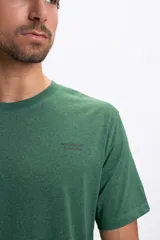 Remera de manga corta color verde jaspeado con un estampado gráfico en la espalda que simula dos casetes de audio apilados.