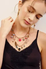 Collar doble de cadena dorada con múltiples dijes colgantes, incluyendo corazones, estrella, símbolo de la paz, cerezas y lunas.