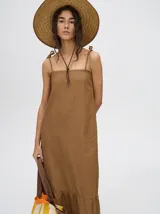 Vestido midi de denim color marrón, con corte holgado, breteles finos con lazos ajustables y detalle de volado en el ruedo.
