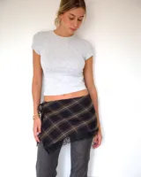 Kilt o falda envolvente corta a cuadros en tonos oscuros, con detalle de encaje negro en el ruedo y cierre lateral con lazo.