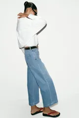 Jeans de tiro alto con pernera ancha y corte cropped. Presenta diseño de cinco bolsillos, cierre frontal con cremallera y botón, e incluye un cinturón oscuro con hebilla metálica.