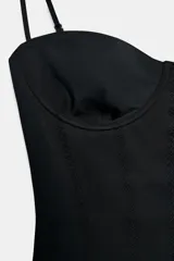 Body negro con escote corazón y tirantes finos ajustables. Presenta un sutil patrón de tejido en relieve vertical y detalle de entredós a tono en el cuerpo. Cierre inferior con botones a presión.