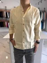Camisa de lino color amarillo pastel con cuello mao, manga larga y botones frontales.