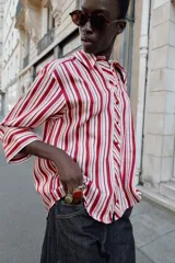 Camisa de cuello solapa con estampado de rayas verticales en tonos rojos, rosas y blancos. Presenta cierre frontal con botones y mangas tres cuartos con puño vuelto.