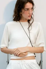 Top blanco de tejido rústico, con cuello redondo y mangas cortas amplias. Bajo recto.