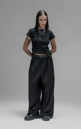 Pantalón sastrero de corte oversize, color negro, con pinzas frontales que forman tablones profundos, cintura ancha, presillas robustas y bolsillos laterales y traseros tipo ojal.