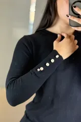 Buzo de hilo negro con cuello redondo, manga larga y detalle de botones decorativos en los puños y a lo largo del antebrazo.