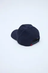 Gorra de pana azul marino con visera curva, parche frontal con texto y pequeño bordado rojo en el lateral.