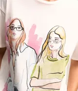 Remera de algodón color blanco con estampado de figuras femeninas de colores. Tiene cuello redondo y mangas cortas.