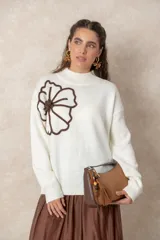 Cartera tipo baguette de diseño minimalista, confeccionada en una combinación de gamuza color beige en el panel frontal y cuero color chocolate en los bordes y la correa. Incluye un detalle colgante de cuentas de madera y cierre superior.