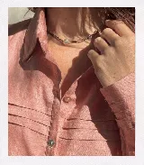 Camisa rosa de lino, con cuello clásico, cierre frontal con botones y tablillas verticales en el frente.