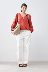 Remera de estilo boho color terracota, con escote en V, cordones decorativos y detalles bordados en los hombros. Presenta mangas largas abullonadas con puños elásticos.