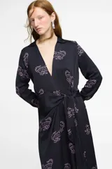 Vestido largo estilo camisero confeccionado en seda viscosa color negro con estampado de tigres en color rosa. Tiene cuello camisero, mangas largas, corte cruzado y lazo en la cintura.