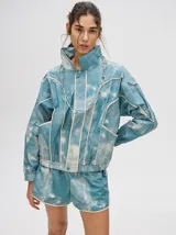 Short de estilo deportivo con pretina elástica, confeccionado en tela satinada con estampado tipo tie-dye en tonos azul y blanco. Presenta bordes con vivo en color crema y un pequeño logo bordado en la parte inferior.