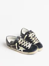 Zapatilla Golden Goose modelo Super-Star de estilo urbano con efecto desgastado. Presenta cuerpo de cuero blanco, estrella lateral con glitter plateado, talón en tono gris texturizado y forro interior de corderito sintético.
