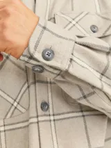 Sobrecamisa de manga larga con cierre frontal de botones y dos bolsillos con solapa en el pecho. Presenta un diseño de cuadros en tonos neutros y corte regular.