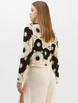 Buzo de tejido crochet con diseño de motivos circulares en contraste blanco y negro, con apliques de pedrería en el centro de los círculos. Presenta corte recto, cuello redondo y manga larga.
