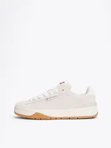 Zapatillas Tommy Jeans de corte bajo, color gris claro, confeccionadas en ante con interior de poliéster y suela de goma color caramelo. Presentan cordones blancos, logo de la marca en la lengüeta y etiqueta de Tommy Jeans en el lateral.