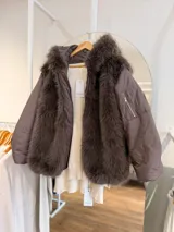 Campera puffer de corte oversize color marrón, con paneles frontales de pelo sintético suave y capucha integrada. Presenta mangas acolchadas con bolsillo lateral con cierre, cierre frontal y diseño abrigado.