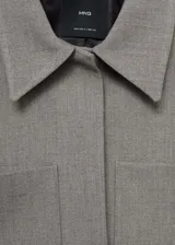 Chaqueta corta de diseño recto y estilo sastrero, confeccionada en tejido fluido color gris. Presenta cuello camisero, cierre frontal con botones ocultos y dos bolsillos de parche en el frente.