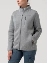 Buzo polar de mujer con cierre frontal completo, cuello alto, bolsillo vertical en el pecho y bolsillos laterales, todos con cierre. Confeccionado en tejido técnico de fibras recicladas con terminaciones elásticas.